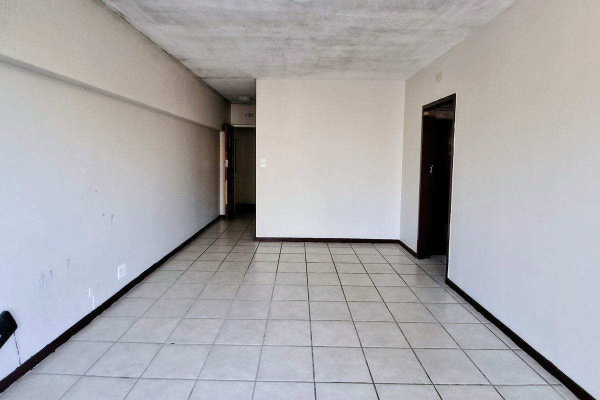 An empty, open-plan living area featuring ceramic floor tiles and neutral walls, requiring cosmetic updates to the ceiling and finishes.