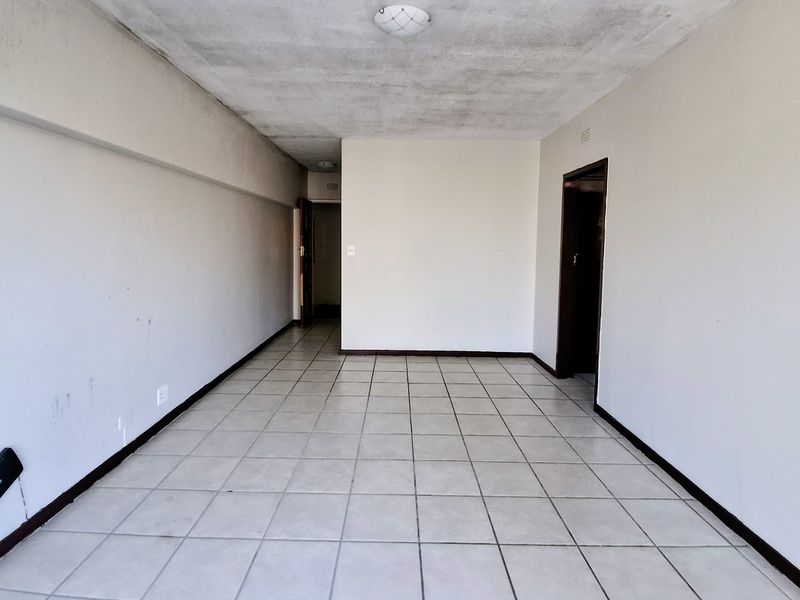 An empty, open-plan living area featuring ceramic floor tiles and neutral walls, requiring cosmetic updates to the ceiling and finishes.