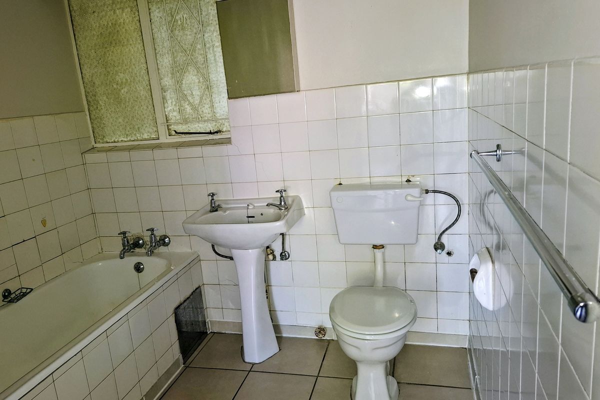 A dated bathroom featuring a pedestal basin, bathtub, and toilet with white wall tiles and tiled flooring, requiring modernization.
