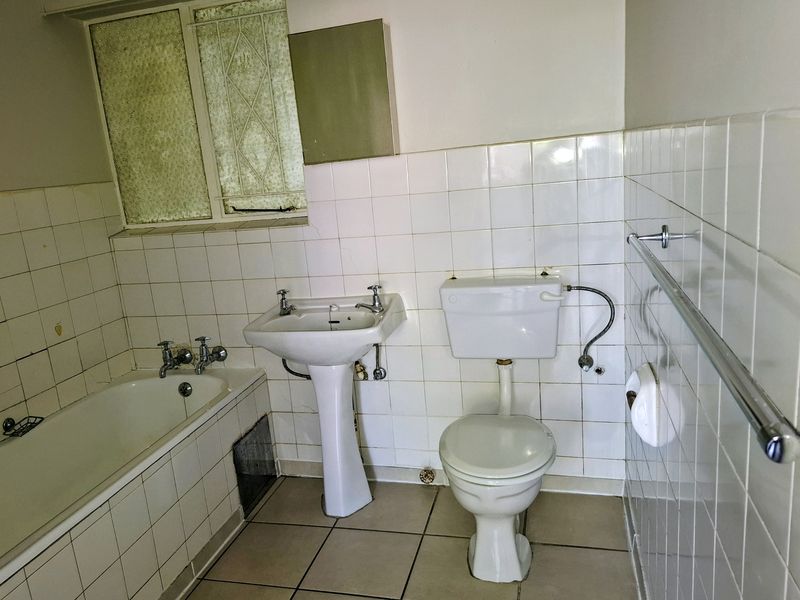 A dated bathroom featuring a pedestal basin, bathtub, and toilet with white wall tiles and tiled flooring, requiring modernization.