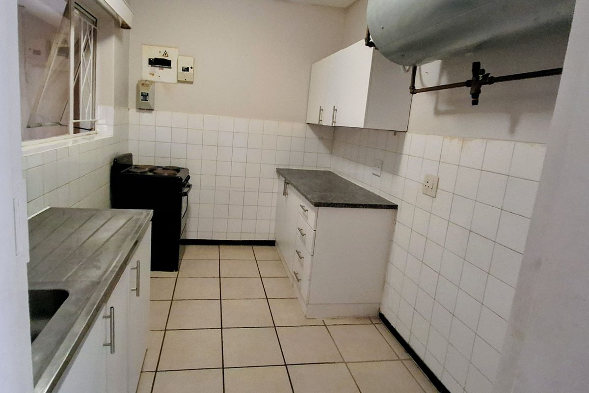 A functional kitchen featuring white cabinetry, laminate countertops, ceramic tiling, and an integrated electric stove, providing a practical space for culinary activities.