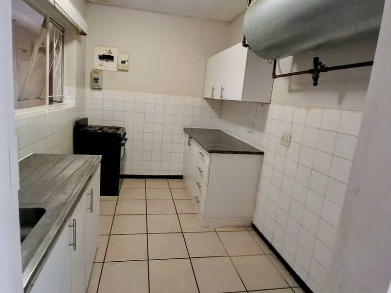 A functional kitchen featuring white cabinetry, laminate countertops, ceramic tiling, and an integrated electric stove, providing a practical space for culinary activities.