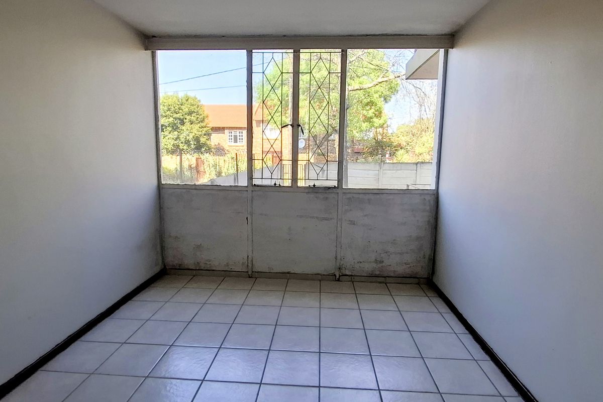 An empty bedroom featuring tiled flooring and a large window with security bars, requiring cosmetic updates to the walls and window frame.