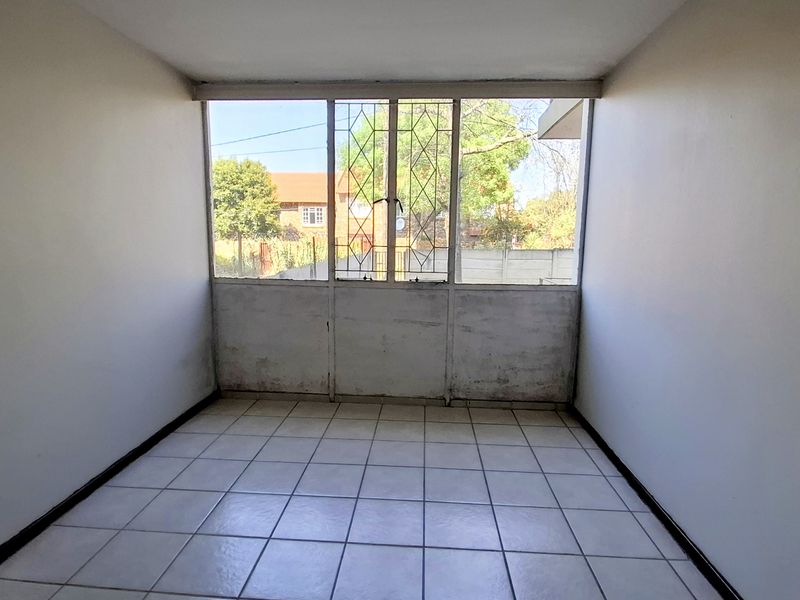 An empty bedroom featuring tiled flooring and a large window with security bars, requiring cosmetic updates to the walls and window frame.