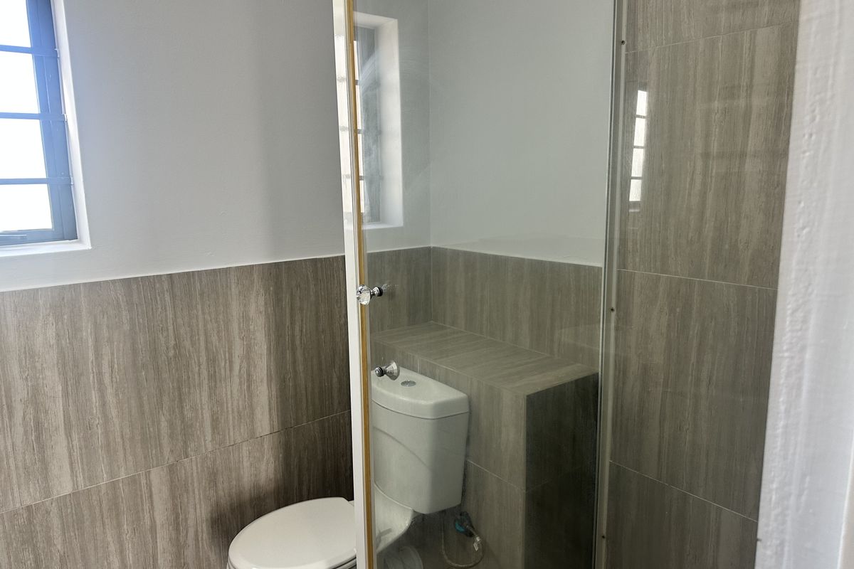 A compact bathroom featuring modern wood-look wall tiles, a white toilet, and a glass shower screen.