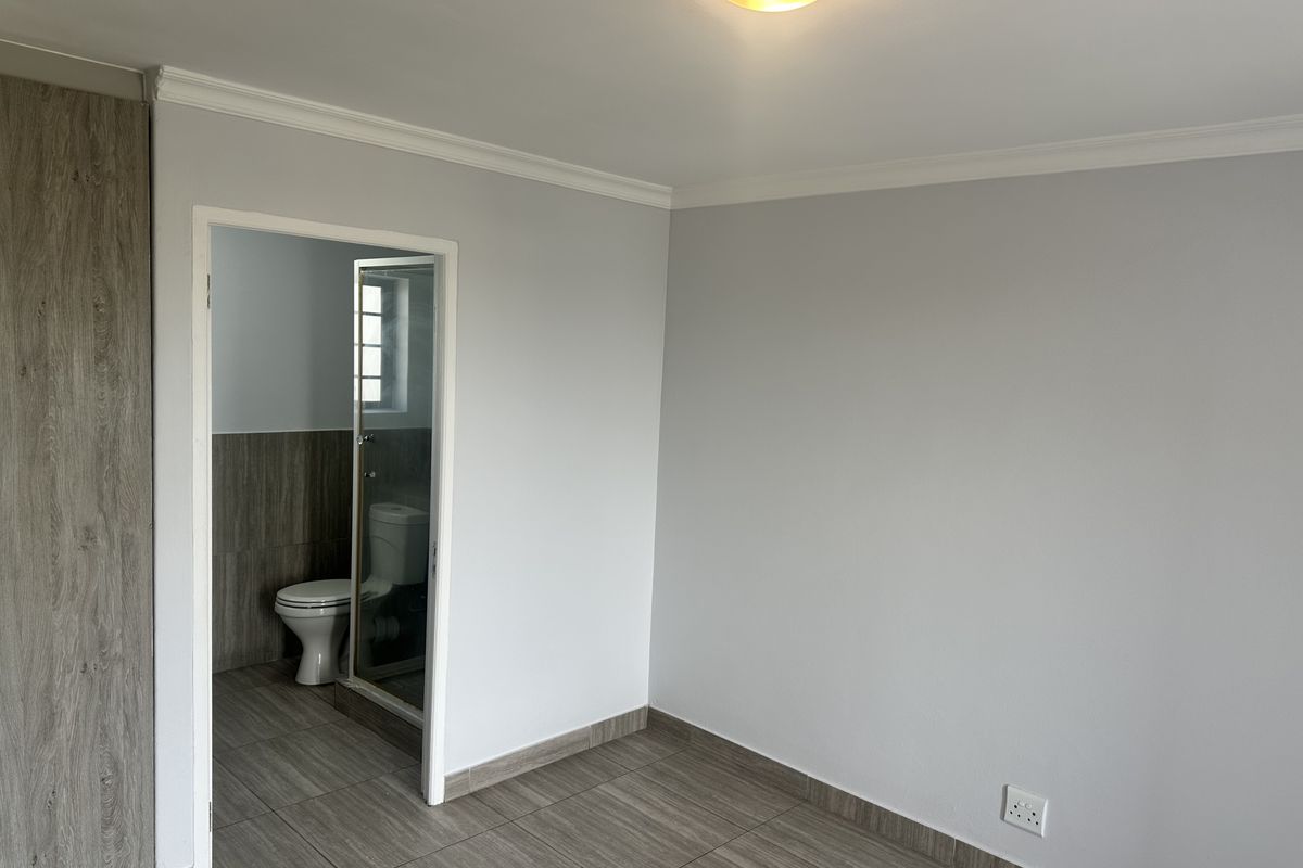A clean, empty bedroom featuring modern wood-look tiled flooring, built-in cabinetry, and direct access to an en-suite bathroom.