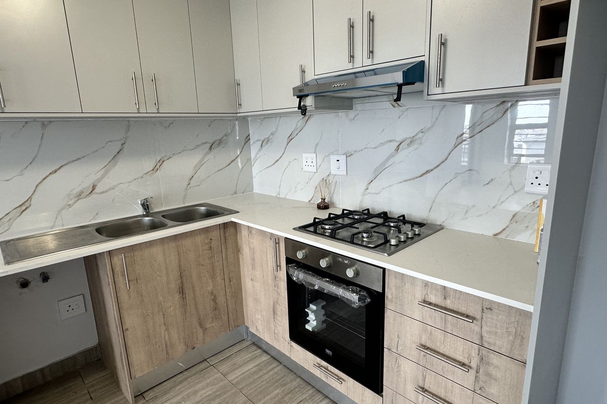 Modern kitchen featuring light wood-finish lower cabinetry, white upper cabinets, stone-look backsplash, gas hob, and built-in oven.