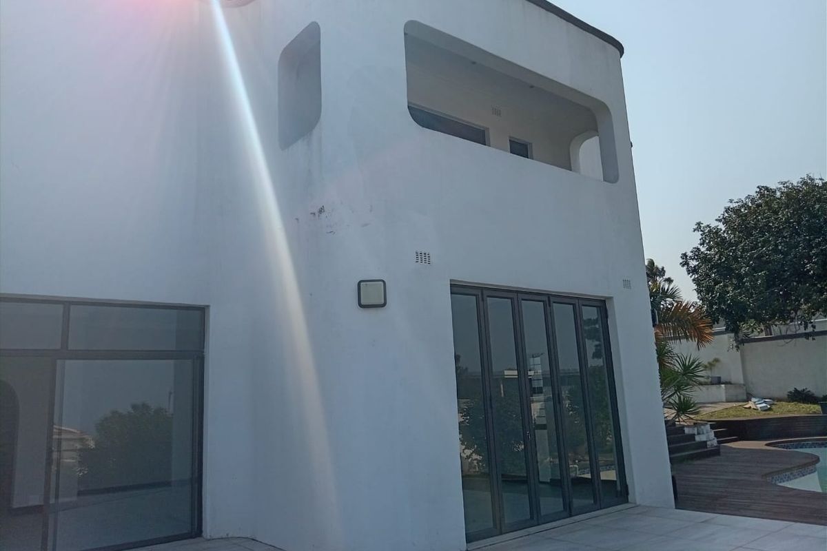 Rear exterior view of the property featuring a tiled patio, bi-fold doors, and an upper-level balcony with modern architectural lines.