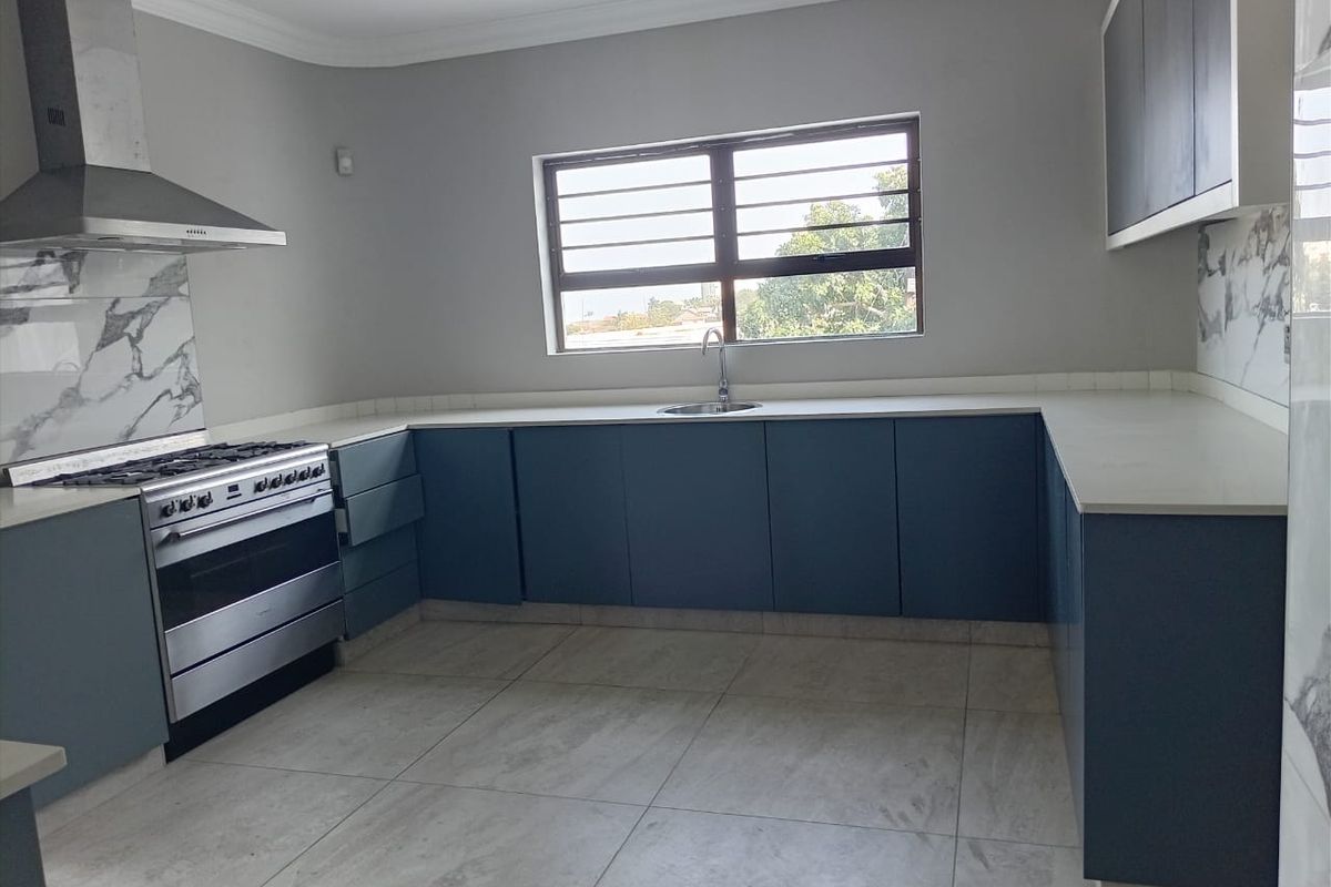 Modern kitchen featuring blue cabinetry, stone countertops, marble-look splashbacks, and a stainless steel gas stove with an extractor fan.