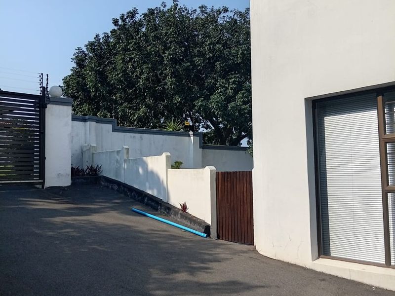 Front exterior view showing the asphalt driveway, perimeter wall with electric fencing, and gated entrance to the property.