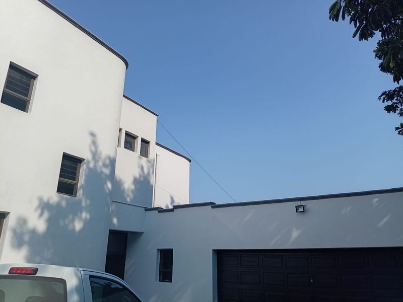 Modern multi-story residential facade featuring clean white rendered walls, dark framed windows, and an integrated garage.