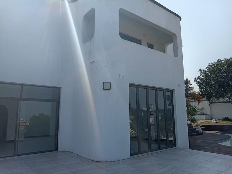 Rear elevation of a modern home featuring bi-fold doors opening onto a tiled patio, with an adjacent swimming pool and wooden decking area.