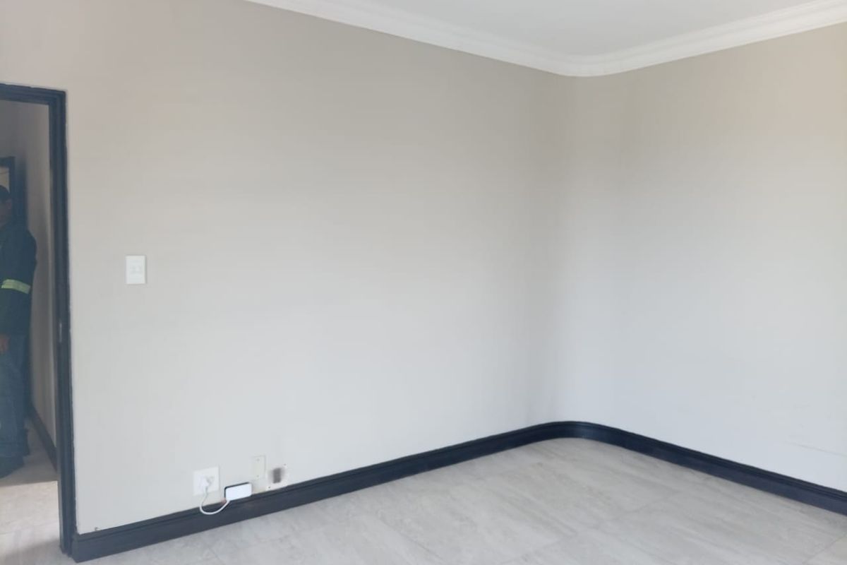 A clean, empty room featuring neutral wall paint, dark contrasting skirting boards, cove cornicing, and modern tiled flooring.