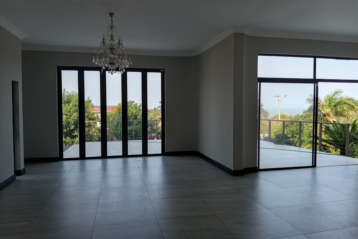 Spacious, light-filled living area featuring large format floor tiles, elegant crystal chandelier, and expansive black aluminium stacking doors opening to an outdoor terrace.