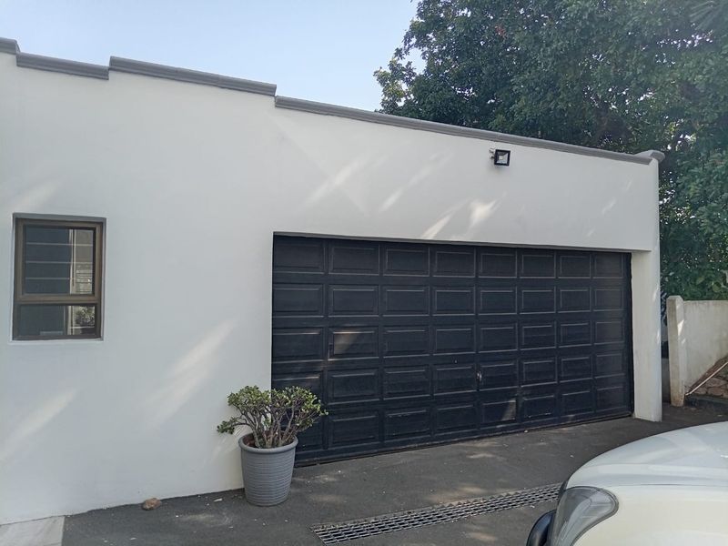 A well-maintained exterior view of a single-car garage featuring a black sectional door, security lighting, and a clean concrete driveway.