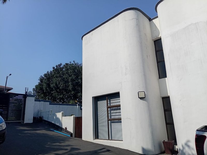 Front exterior view of the property featuring a curved facade, asphalt driveway, and boundary wall with security gate.