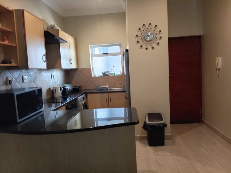 A functional kitchen featuring built-in cabinetry, granite countertops, a tiled backsplash, and tiled flooring, with an adjacent entrance door and intercom system.