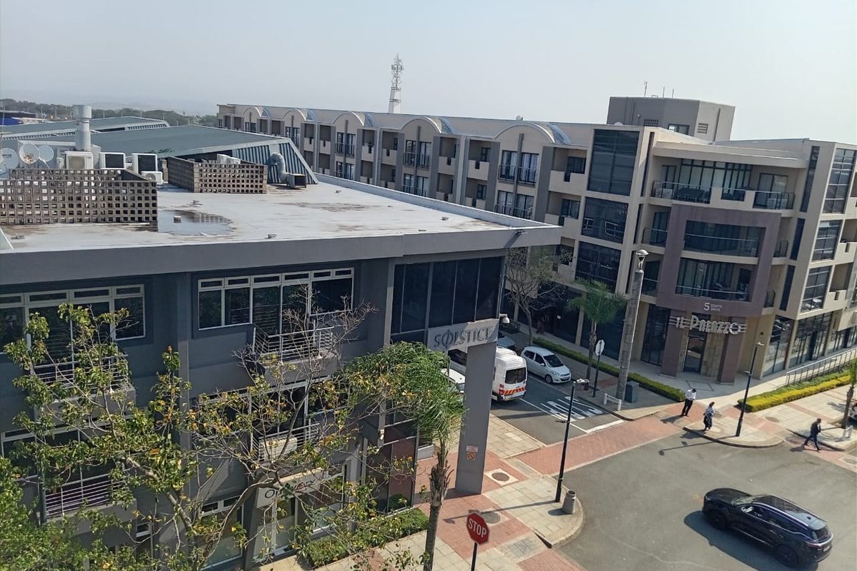 An elevated aerial view of a modern apartment complex and surrounding commercial buildings, featuring paved walkways and street-level access.
