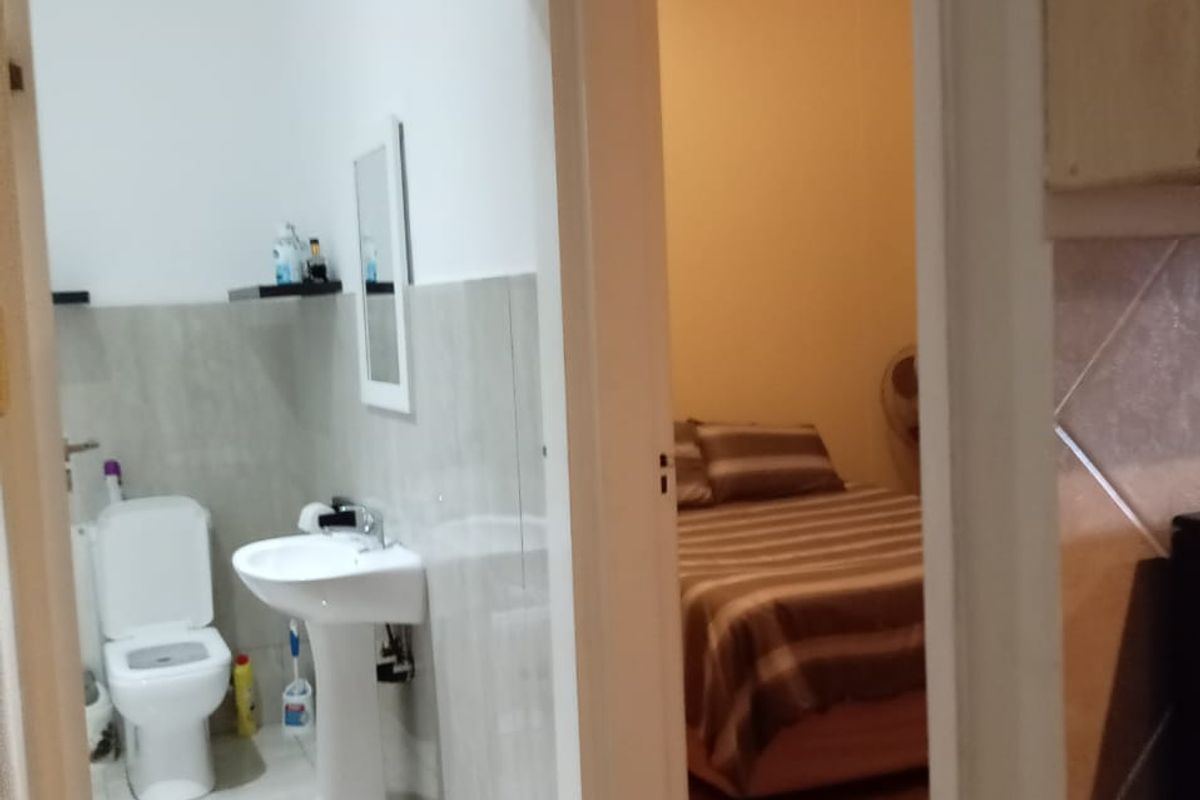 A functional bathroom featuring a pedestal washbasin and toilet, with neutral wall and floor tiling, viewed from an adjacent hallway.