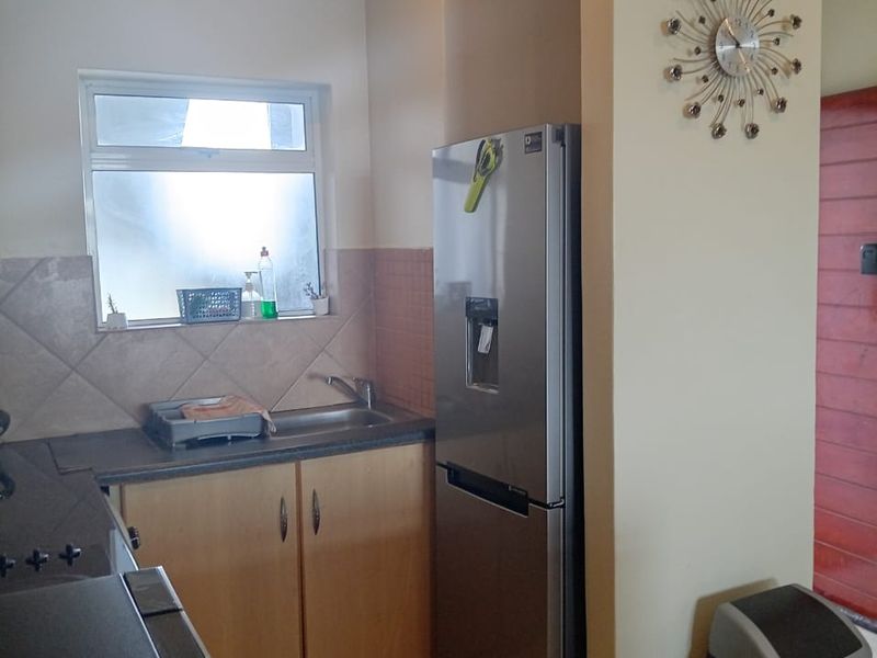 A functional kitchen area featuring built-in cabinetry, laminate countertops, a stainless steel sink, and tiled backsplash with neutral wall finishes.