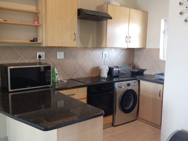 A functional kitchen featuring granite countertops, light wood cabinetry, a tiled backsplash, and built-in appliances including an oven, hob, and washing machine.