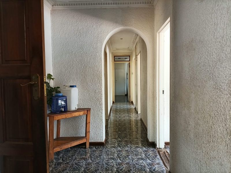 A long interior hallway featuring textured walls, arched architectural detailing, crown molding, and dark patterned floor tiles.