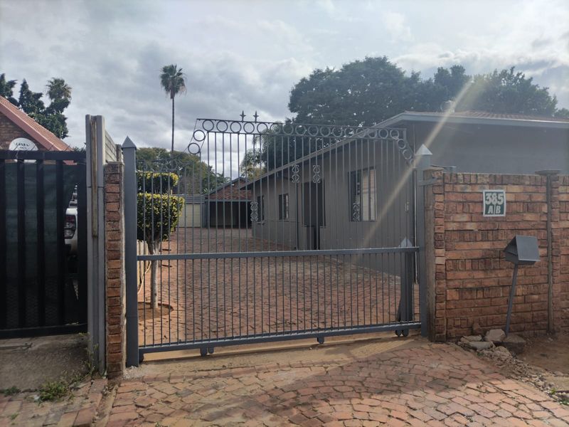 Front view of the property featuring a secure metal sliding gate, brick boundary wall, and a paved driveway leading to the garage.