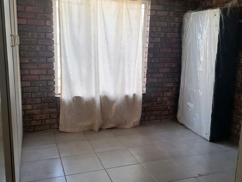A bedroom featuring exposed brick walls, tiled flooring, and a built-in cupboard, offering a blank canvas for renovation or restyling.