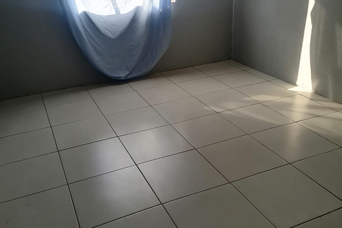 An empty bedroom featuring neutral ceramic floor tiles and natural light from a single window.