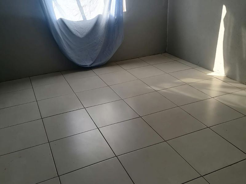 An empty bedroom featuring neutral ceramic floor tiles and natural light from a single window.