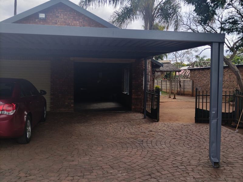 Front exterior view featuring a brick facade, a paved driveway, and a covered carport area with a garage entrance.