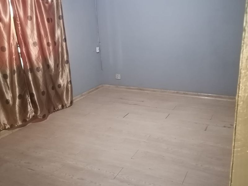 An empty bedroom featuring light-toned laminate flooring and neutral grey walls, providing a blank canvas for interior design.