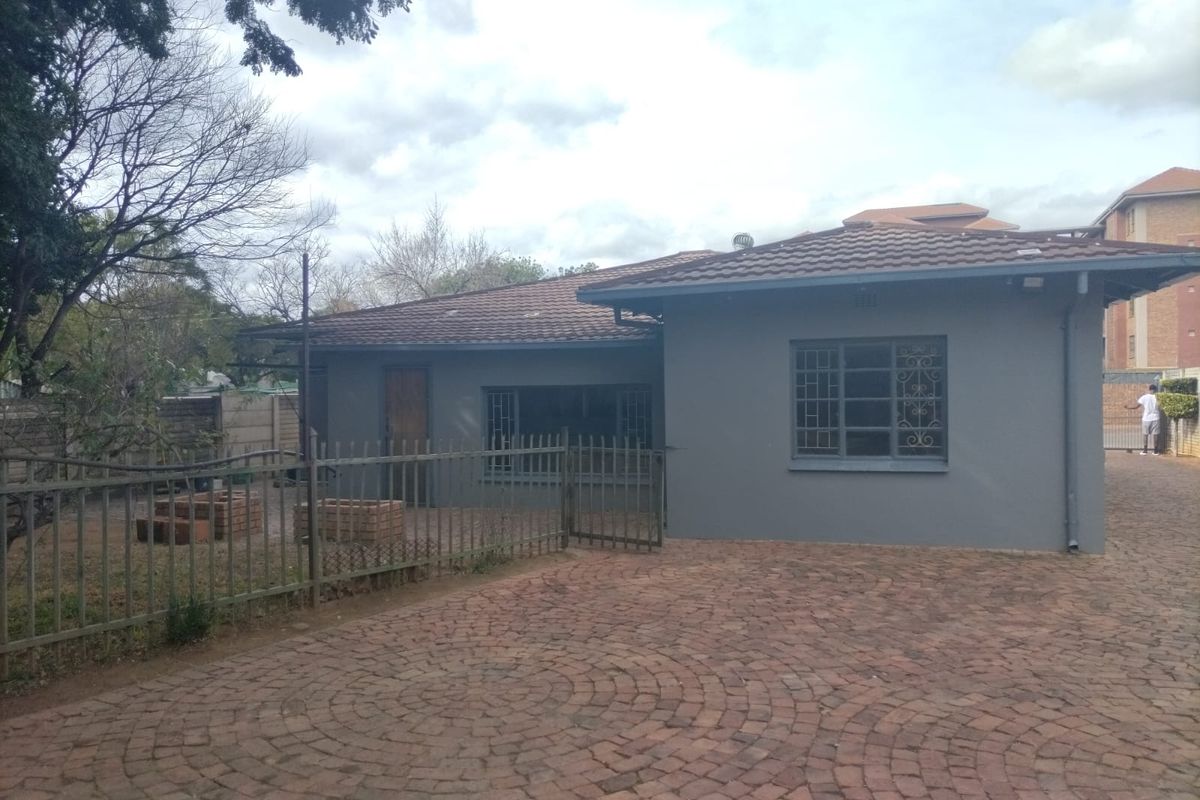 Rear view of the property featuring a paved driveway, tiled roof, and secure metal fencing surrounding the garden area.