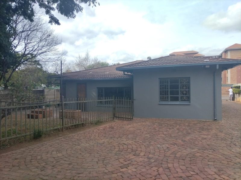 Rear view of the property featuring a paved driveway, tiled roof, and secure metal fencing surrounding the garden area.