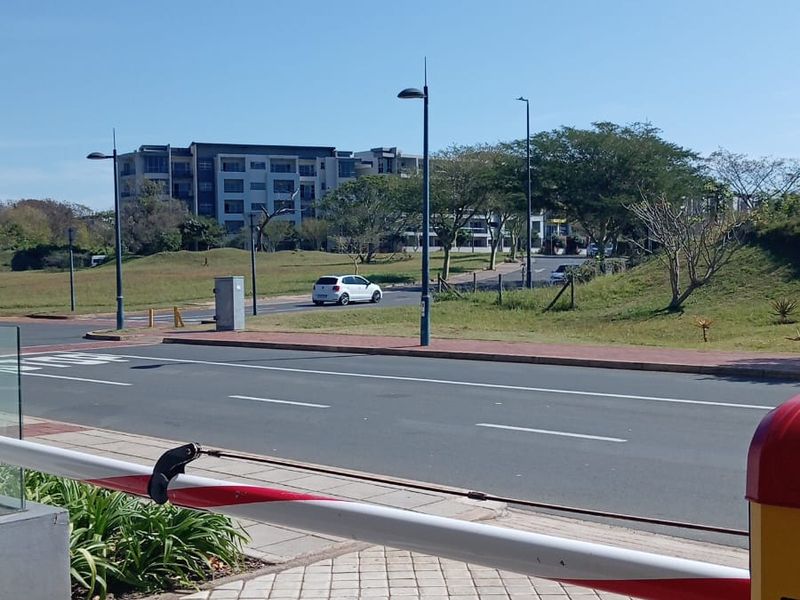 View of the street and surrounding neighbourhood approach from the property entrance, featuring a security boom gate and paved pedestrian access.