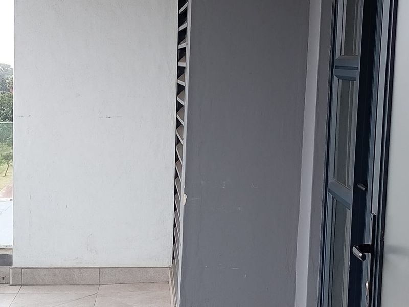 A clean, modern balcony featuring tiled flooring, a dark aluminium framed glass door, and a privacy louvre screen.