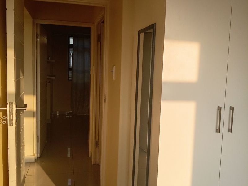 A bright hallway featuring tiled flooring and a built-in cupboard, leading into an adjacent room.