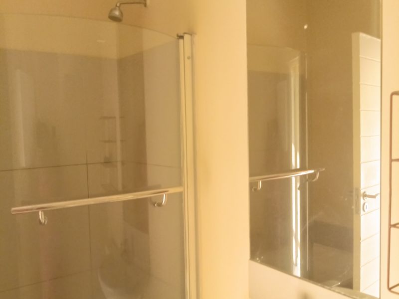 A functional bathroom featuring a curved glass shower enclosure, a wall-mounted basin with a mixer tap, and a large vanity mirror.