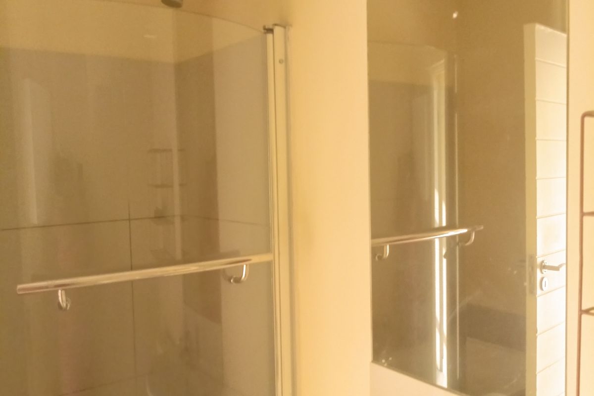 A functional bathroom featuring a curved glass shower enclosure, a wall-mounted basin with a mixer tap, and a large vanity mirror.