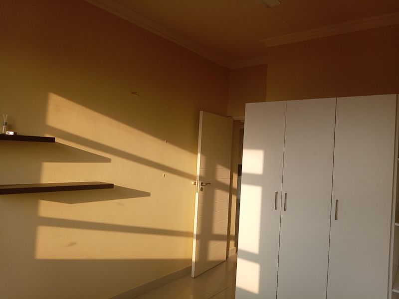 A bedroom featuring a built-in white wardrobe, floating wall shelves, tiled flooring, and a standard internal door with visible wall surface wear.