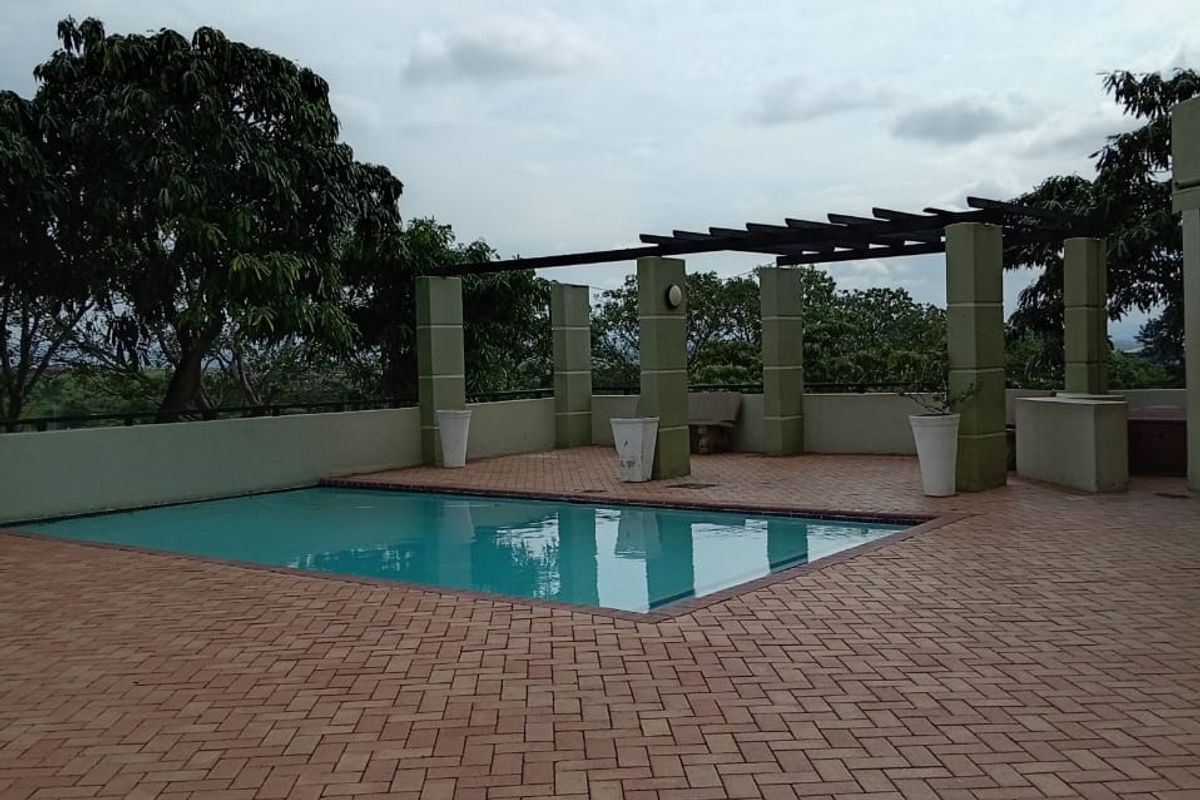 A spacious outdoor pool area featuring brick paving, a pergola structure, and concrete pillars, offering a clean and well-maintained recreational space.