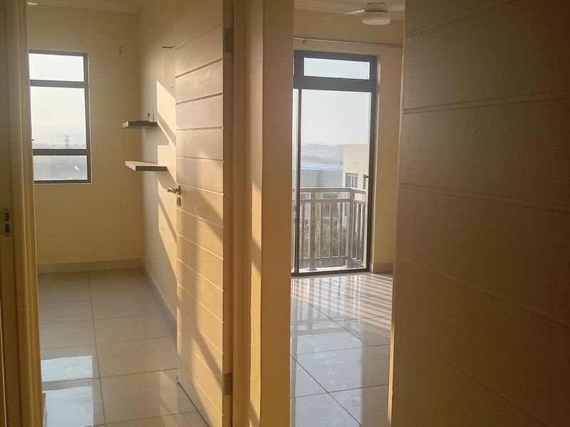 A bright, empty hallway with tiled flooring, leading to a bedroom and a balcony with outdoor views.