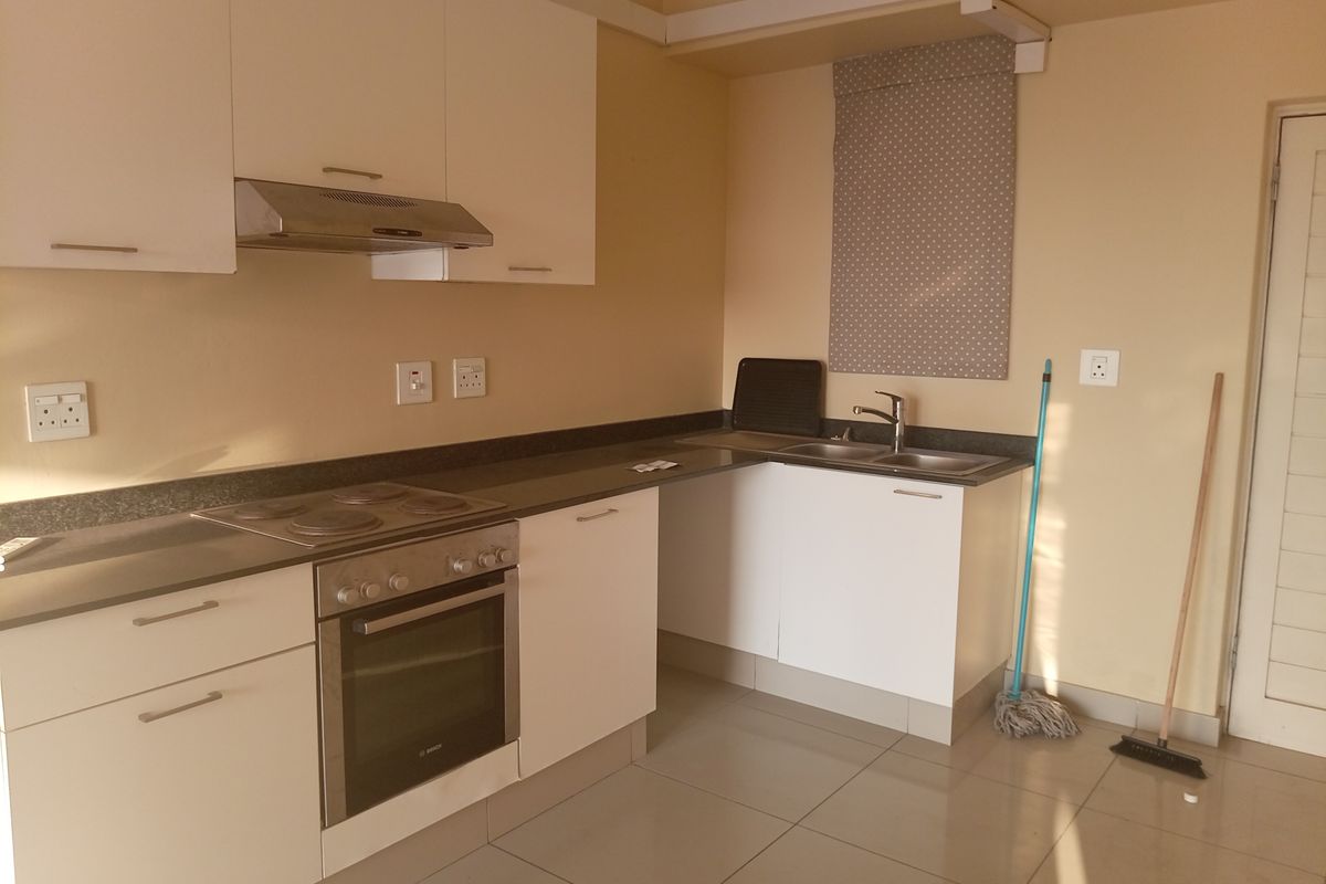A functional kitchen featuring white cabinetry, dark countertops, a built-in oven, electric hob, and stainless steel sink with tiled flooring.