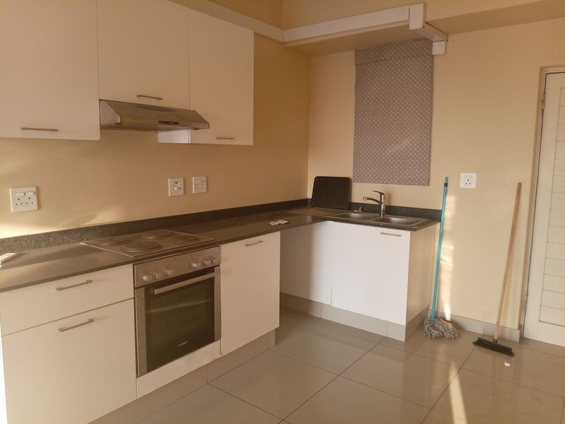 A functional kitchen featuring white cabinetry, dark countertops, a built-in oven, electric hob, and stainless steel sink with tiled flooring.