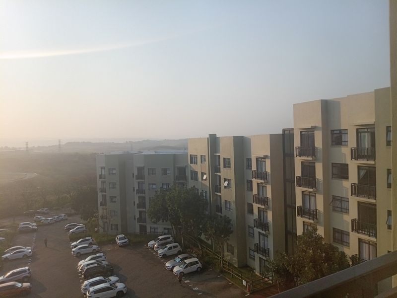 Elevated view overlooking the apartment complex exterior, featuring multiple balconies and an adjacent parking area.