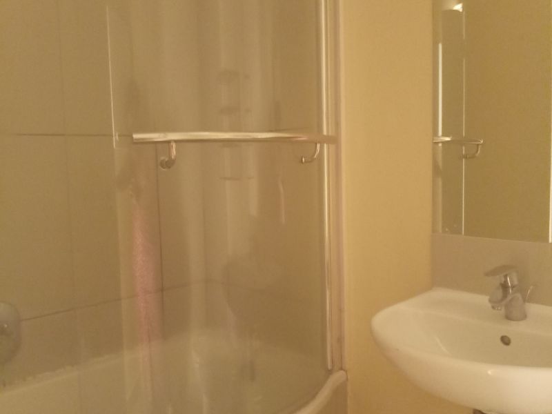 A functional bathroom featuring a wall-mounted basin with chrome fixtures and a shower area enclosed by a curved glass screen.