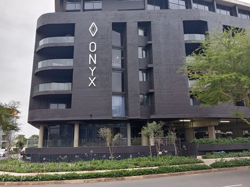Modern multi-story apartment building featuring a dark brick facade, curved glass balconies, and integrated covered parking.