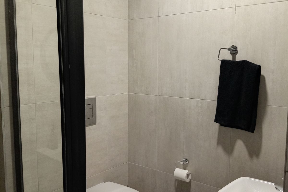 Modern bathroom featuring a wall-mounted toilet, a sleek glass shower enclosure, and a vanity basin with neutral wall and floor tiling.
