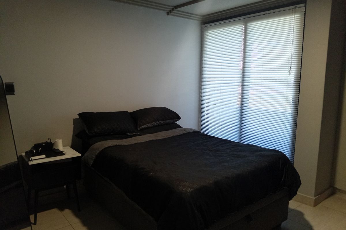 A bedroom featuring tiled flooring, cove molding, and venetian blinds covering the window.