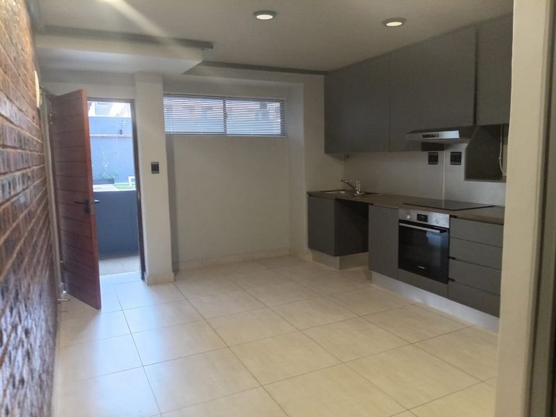 Modern kitchen featuring grey built-in cabinetry, integrated oven and hob, tiled flooring, and an exposed brick feature wall with direct access to the exterior.
